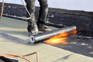 Photo of a roofer applying SBS torch on roofing a commercial Calgary flat roof