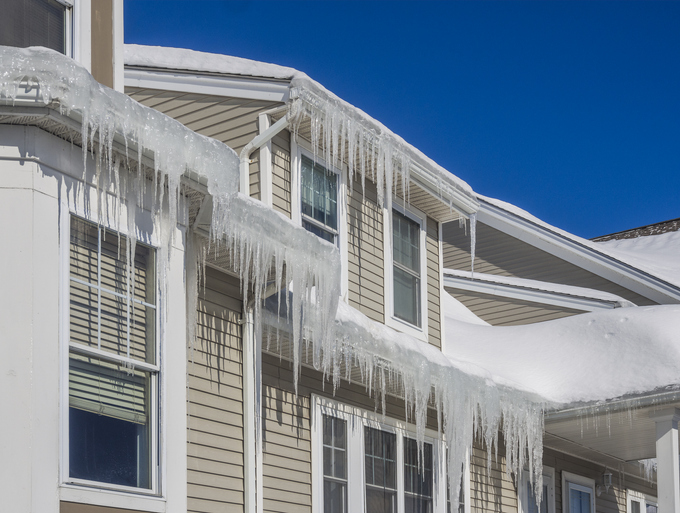 Ice dams and snow on roof and gutters A house covered in snow and icicles